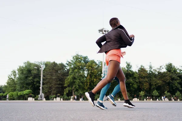 Dos chicas multiétnicas corriendo por las calles de la ciudad, comunicándose al aire libre. — Foto de Stock