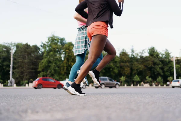 Dos piernas de chicas multiétnicas corriendo por las calles de la ciudad, comunicándose al aire libre. — Foto de Stock