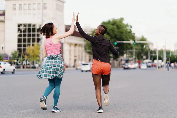 Two multiethnic girls running through the city streets, outdoor communicating. — Stock Photo, Image