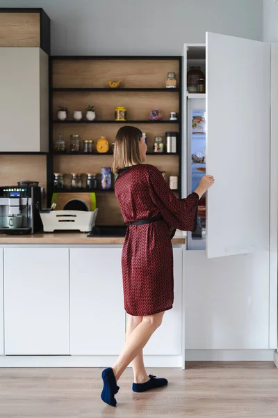 家で冷蔵庫のキッチンで食べ物を探している空腹の女性 — ストック写真