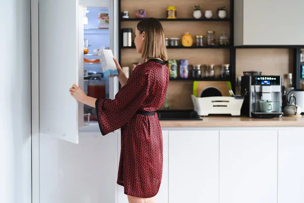 Hongerige vrouw op zoek naar voedsel in de koelkast keuken thuis — Stockfoto