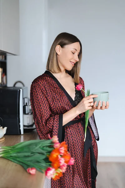 Mulher tomando um café em casa enquanto aprecia flores — Fotografia de Stock