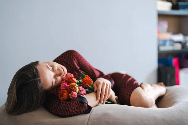 若い女性は柔らかい豆の袋でリラックスして家で花を楽しむ — ストック写真