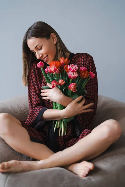 Молодая женщина наслаждается цветами дома расслабляясь на мягкой бобовой сумке — стоковое фото