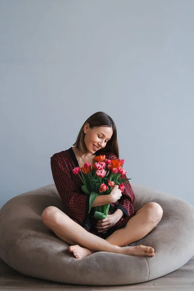 Junge Frau genießt Blumen zu Hause entspannt auf einem weichen Bohnensack — Stockfoto