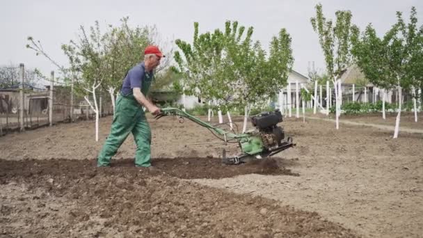 Чоловік орає землю в саду на фоні неба — стокове відео