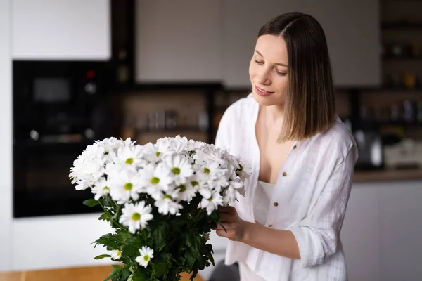Красива жінка кладе свіжі білі квіти у вазу — стокове фото