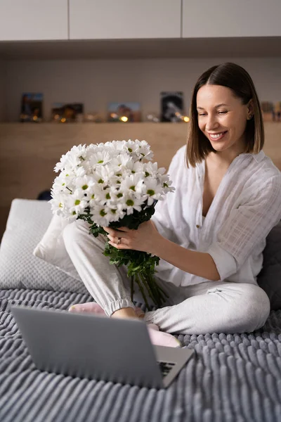 Donna che comunica usando un computer portatile mentre dichiara sulla scommessa con un mazzo di fiori bianchi — Foto Stock