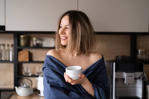 Νυσταγμένη γυναίκα πίνει καφέ το πρωί στην κουζίνα. — Φωτογραφία Αρχείου