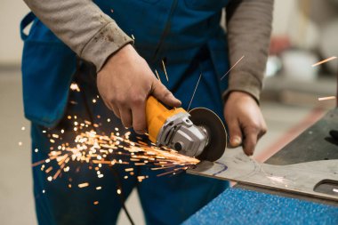 Kıvılcımlı metal üzerinde dairesel bir değirmenle çalışan bir işçi.