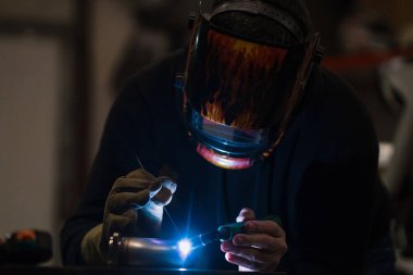 Garajda argon kaynak makinesiyle çalışan bir adam.