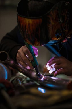 Garajda argon kaynak makinesiyle çalışan bir adam.