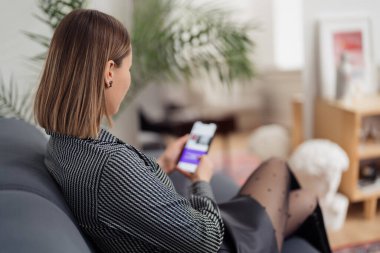 Kanepede otururken telefonu elinde tutan kadın.