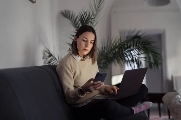 Жінка використовує ноутбук під час введення телефону у вітальні — стокове фото