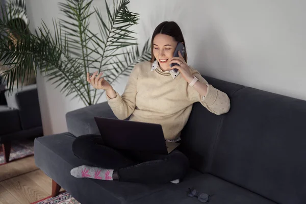 リビングルームで電話をしながらノートパソコンを使う女 — ストック写真