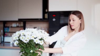 Güzel bir kadın vazoya taze beyaz çiçekler koyar.