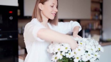 Güzel bir kadın vazoya taze beyaz çiçekler koyar.