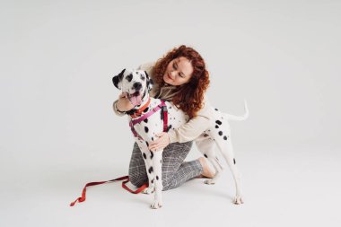 Beyaz arka planda dalmaçyalı köpeğiyle poz veren bir kadın.