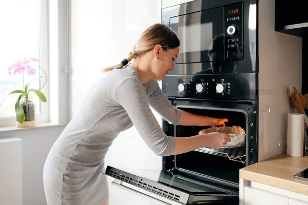 Jonge vrouw zet de zelfgemaakte taart in de oven — Stockfoto