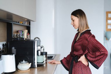 Evde kahve yapmak için kahve makinesi kullanan bir kadın. Evde latte hazırlarken ipek bornoz giyen bir kadın.