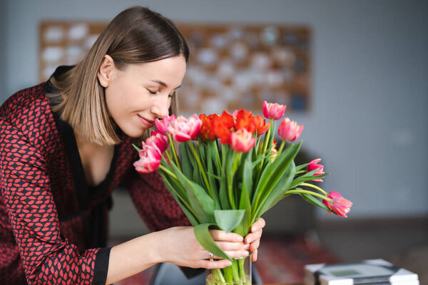 Beautiful woman arranging flowers presented by her husbant at home, happy and joyful