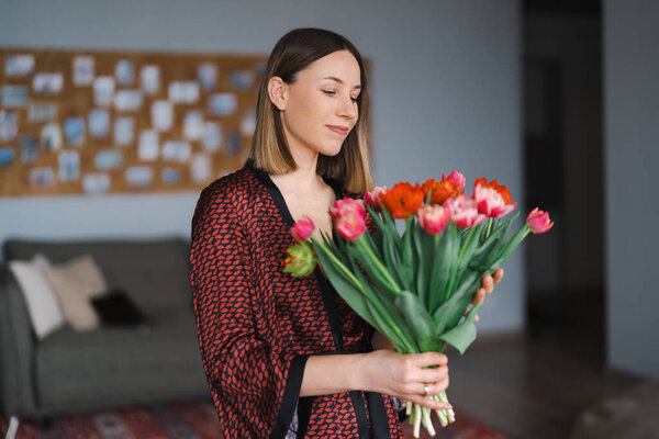 Happy woman enjoy bouquet of tulips. Housewife enjoying a bunch of flowers and interior of kitchen. Sweet home. Allergy free