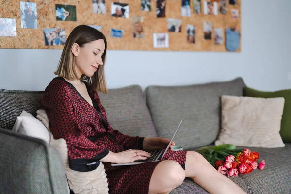 Woman wearing a silk robe using laptop at home relaxing, sitting on a couch