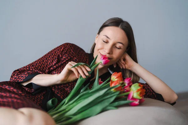 幸せな女性はチューリップの花束を楽しむ 快適な豆袋でリラックスしながら 主婦は花の束を楽しんでいます いい家だ アレルギーフリー — ストック写真