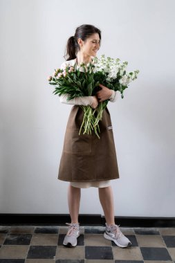 Beyaz arka planda bir demet beyaz ve pembe çiçeği kucaklayan çiçekçi kadın.