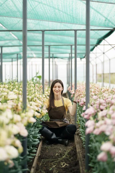 Pretty women relaxing among flowers while sitting in a meditation pose in the green house