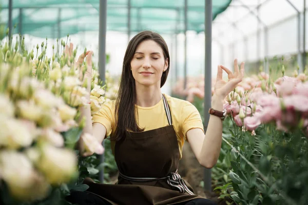 Pretty women relaxing among flowers while sitting in a meditation pose in the green house