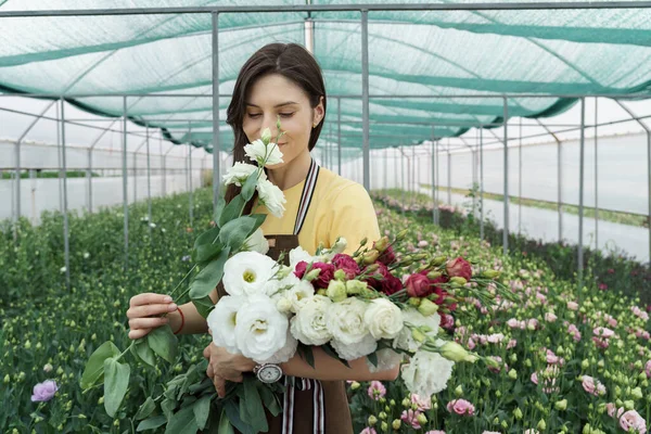 Woman florist has an order for fresh flowers. She makes a beautiful bouquet in the green house.
