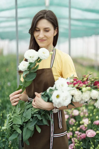 Woman florist has an order for fresh flowers. She makes a beautiful bouquet in the green house.