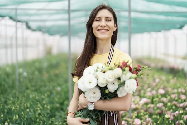 Woman florist has an order for fresh flowers. She makes a beautiful bouquet in the green house.