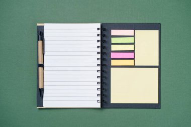 Kağıt yeşili arka planda okul defteri, sarmal not defteri ve karton kalem.