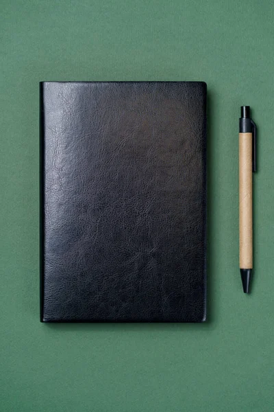 Black leather notebook on a paper green background, notepad mock up, top view shot