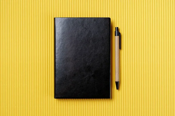 Black leather notebook on a paper yellow background, notepad mock up, top view shot