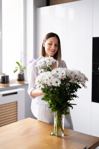 Ευτυχισμένη Και Χαρούμενη Νεαρή Γυναίκα Άσπρα Λουλούδια Τακτοποιεί Στο Σπίτι — Φωτογραφία Αρχείου