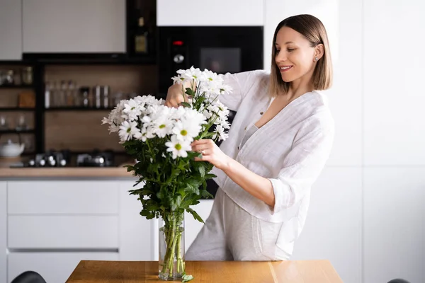 Ευτυχισμένη Και Χαρούμενη Νεαρή Γυναίκα Άσπρα Λουλούδια Τακτοποιεί Στο Σπίτι — Φωτογραφία Αρχείου