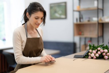 Kadın, dükkanda çalışırken hediye kutusuna pul yapıştırıyor. Sipariş için hazırlanın.