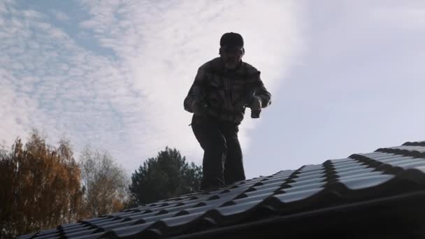 Roofer met twee schroevendraaiers loopt op een metalen dak zonder verzekering. — Stockvideo