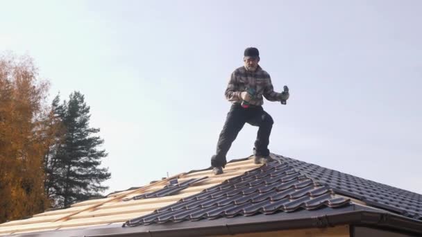 Roofer met twee schroevendraaiers loopt op een metalen dak zonder verzekering. — Stockvideo