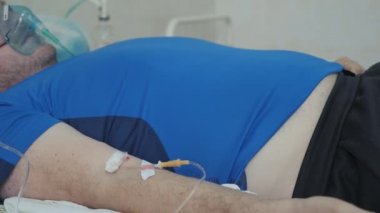 Hastane yatağında hasta bir adam. Koluna damar içi damlalar yerleştirildi. Oksijen maskesinin yüzünde. Oksijen zengini solunum.