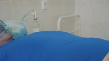 Hastane yatağında hasta bir adam. Koluna damar içi damlalar yerleştirildi. Oksijen maskesinin yüzünde. Oksijen zengini solunum.