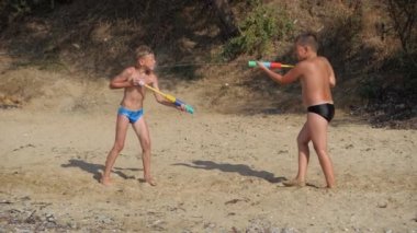 Çocuklar deniz sahilinde su tabancalarıyla oynuyorlar..