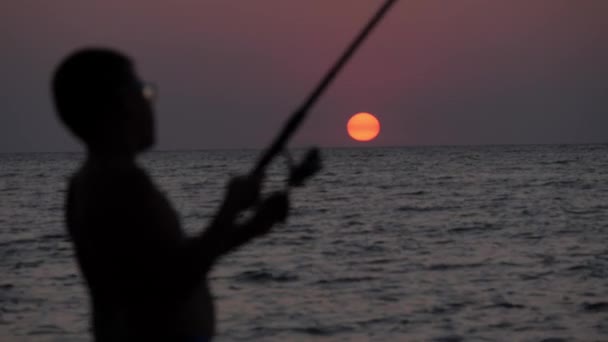 海の夕日を背景に釣竿を持つ子供のシルエット。海釣り. — ストック動画