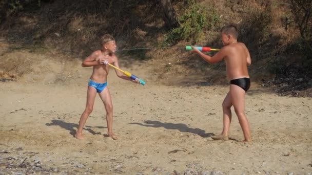 남자 아이들은 바닷가에서 물총을 가지고 놀고 있다. — 비디오