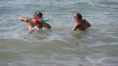 Çocuklar denizde su tabancalarıyla oynarlar..
