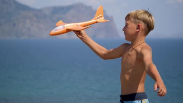 바다 배경에 손에 장난감 비행기를 들고 있는 소년. — 비디오