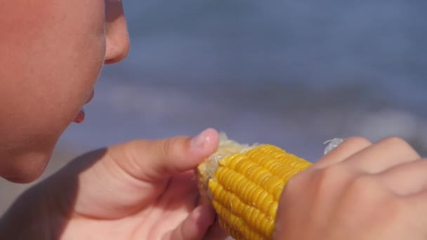 Bambino mangia mais sulla riva del mare. — Video Stock